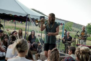 A performer plays music for seated audience members under a large outdoor tent.