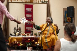 A lively performer in a yellow robe gestures enthusiastically during an indoor presentation.