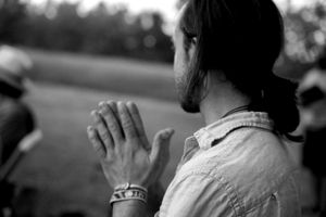 A person clasps their hands together in prayer position while wearing a white shirt in a black and white photograph.