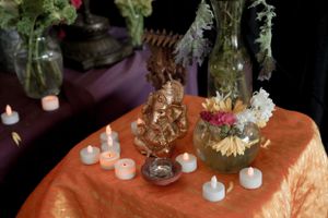 Altar decorated with flowers, candles and crystals on orange tablecloth.