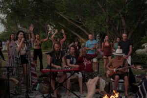 A lively outdoor music performance with musicians and dancing crowd around a campfire.