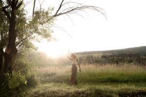 A silhouette stands in a golden meadow at sunset with trees framing the scene.