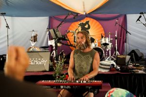 A musician performs at a keyboard under a decorated tent with vibrant lighting.