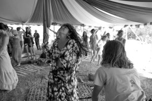 Black and white photo of people dancing at a lively event under a fabric-draped tent.