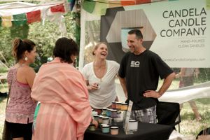 Candela Candle Company booth with customers browsing products at an outdoor market.