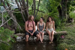 Friends sitting together on a log by the water's edge during a summer gathering.