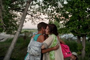 Two people share an intimate moment outdoors at dusk under trees.