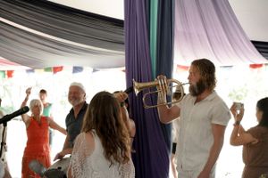 Musicians and performers gather under a draped tent ceiling during a lively celebration.