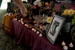 Memorial altar with candles, flowers and photographs on burgundy tablecloth.