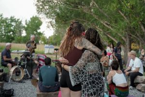 People embracing at an outdoor gathering with musicians performing in the background.