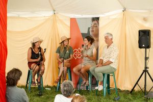 A panel discussion takes place in a cream-colored festival tent with audience members seated.