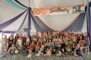 Large group photo of festival attendees gathered under a decorated tent with Sanctuary banner.