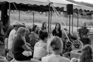 Musicians perform under a tent canopy for a seated audience at an outdoor festival.