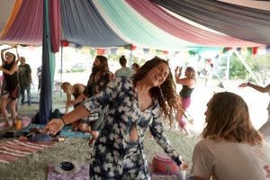 People dancing and celebrating under colorful fabric decorations at an outdoor gathering.