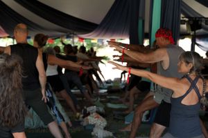 People stretch their arms forward during a group exercise class under draped fabric.