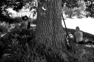 A black and white photo of people resting near a large tree trunk.