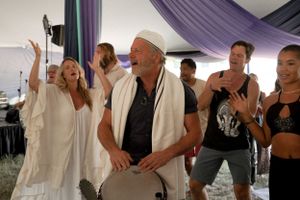 Group of people dancing and celebrating under a purple draped tent at a festival.