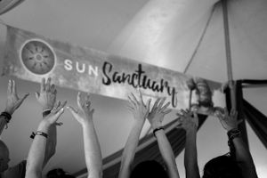 Black and white image of raised hands reaching up toward a Sun Sanctuary banner.