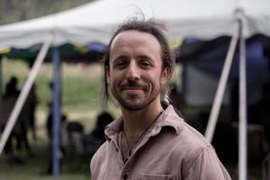 A person wearing a pink button-up shirt smiles under a white tent.