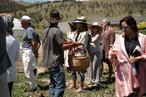 A group gathers outdoors on a sunny day with mountains visible in the background.