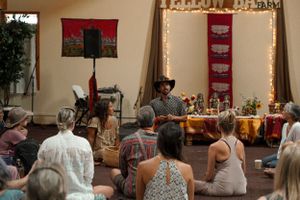 An indoor gathering with audience members watching a performance in a room decorated with red tapestries and string lights.