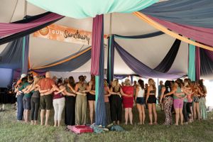 Large group of festival participants gather in a circle under a decorated tent with colorful draping.