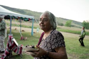 Woman enjoying outdoor festival carries a plate of food under tent canopy.