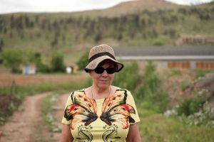 Someone wearing sunglasses and straw hat stands on dirt path with mountains in background.