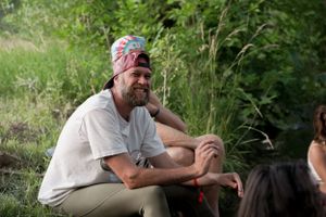 Person with a beard and bandana sits outdoors during a summer gathering.