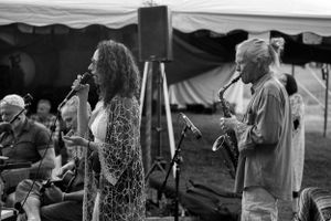 Musicians perform on stage during a black and white outdoor concert scene.