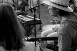 Musician performs at an outdoor venue wearing a wide-brimmed hat in black and white.