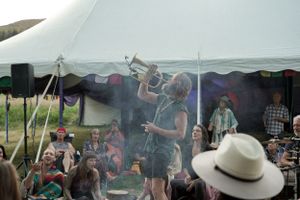 Performer on stage during sunset at outdoor music festival with crowd visible.