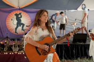Musician performing with an acoustic guitar under a decorated festival tent with colorful banners.