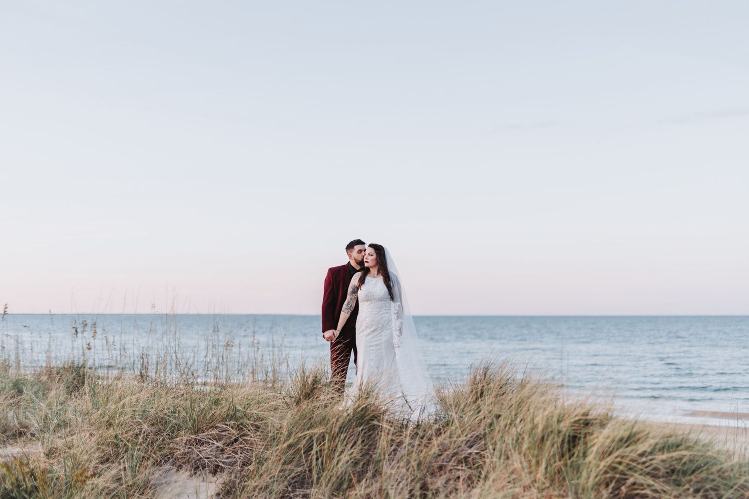Newlyweds share a romantic moment outdoors under white pillars with string lights at dusk during their wedding celebration.
