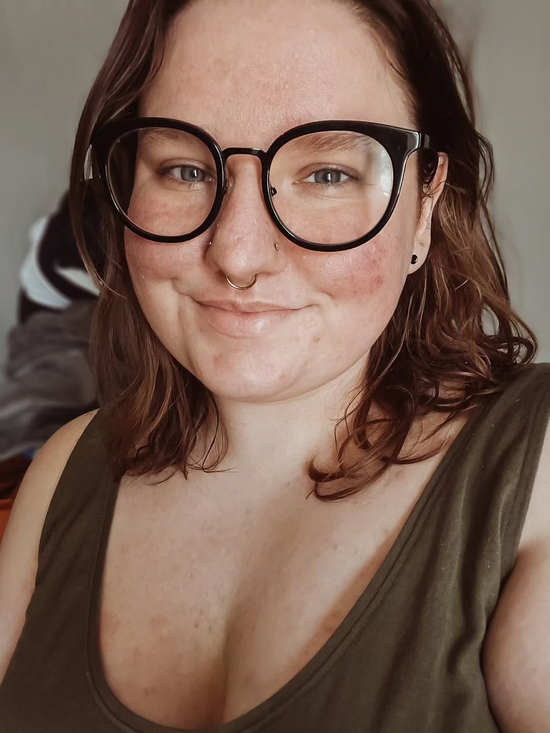 Casual self-portrait of someone wearing round glasses and an olive green tank top.