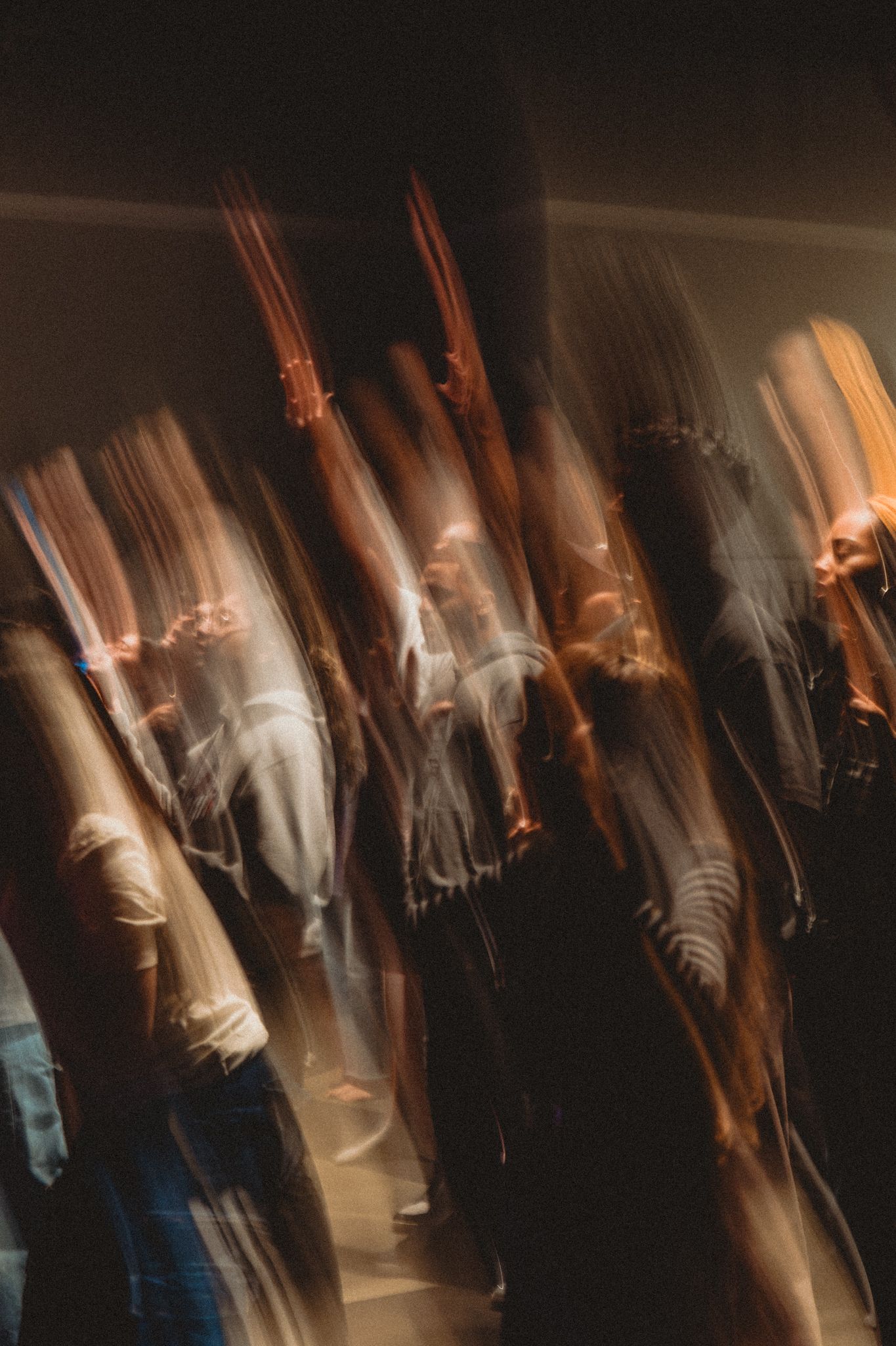 Blurred motion photography of crowd of people dancing in dark venue with long exposure effect.