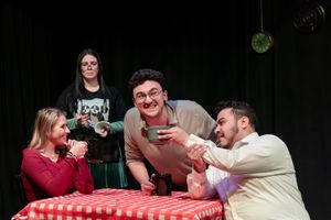 Four actors perform a scene around a red checkered tablecloth.