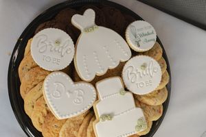 Decorated sugar cookies with white icing arranged on a dark plate with chocolate chip cookies.