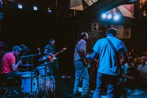 Wide shot of musicians performing on dark stage with blue spotlights.