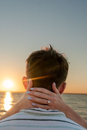 Person looking at ocean sunset with hands behind head in silhouette against golden sky.