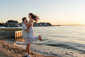 Couple walking along beach shoreline during golden sunset with waves lapping at their feet.