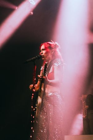 Rock musician performing on stage with guitar under dramatic pink spotlights.