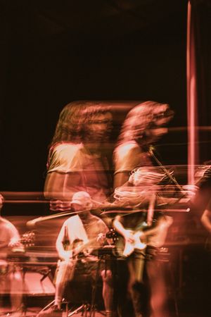 Blurry long-exposure photo of a rock band performing on stage under red lighting.