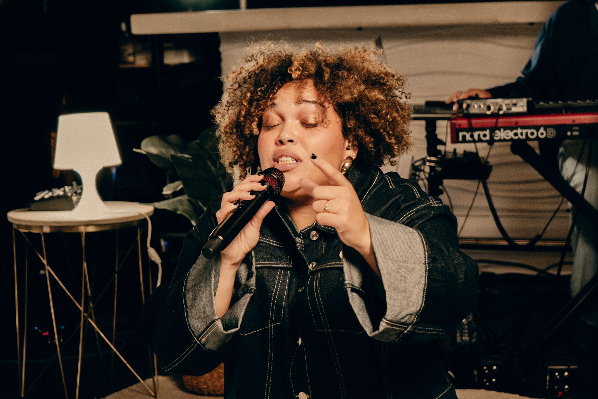 Performer singing passionately on stage with curly hair and dramatic lighting during a live music performance.