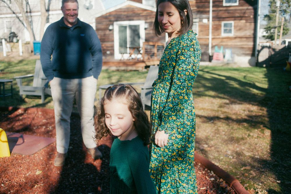 Daughter holds the mother's hand as she looks towards the camera catching the light of the sun during a family session in Portland, Maine.