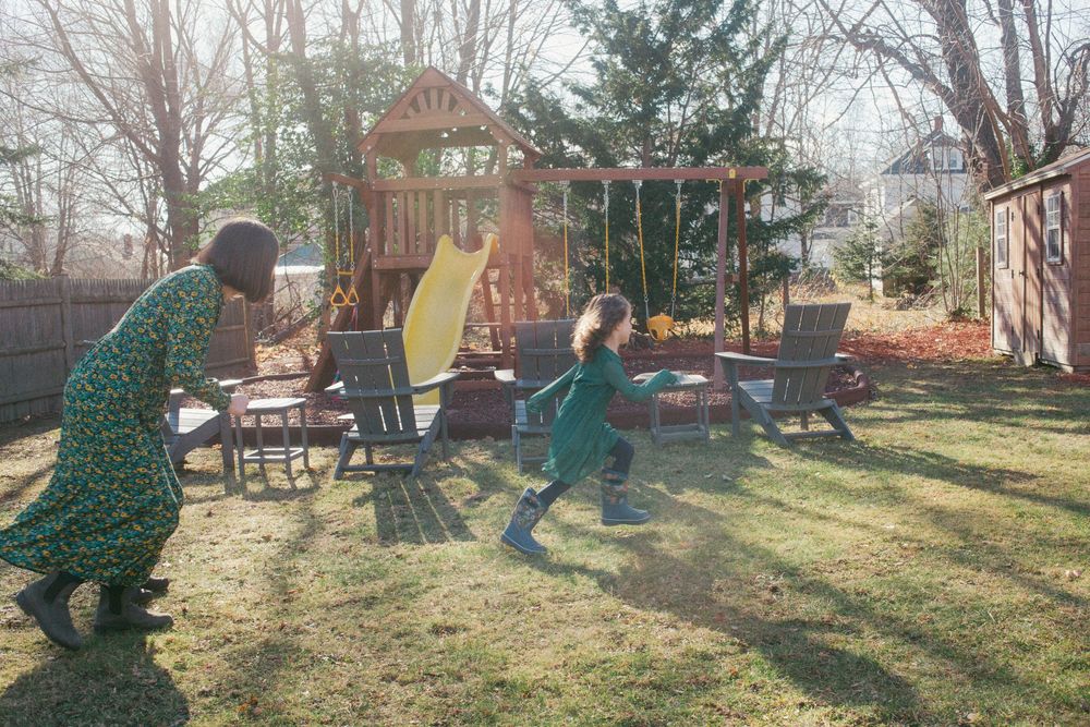 Mother chases daughter around their backyard in green dresses by the swing set in a home in Portland, Maine.