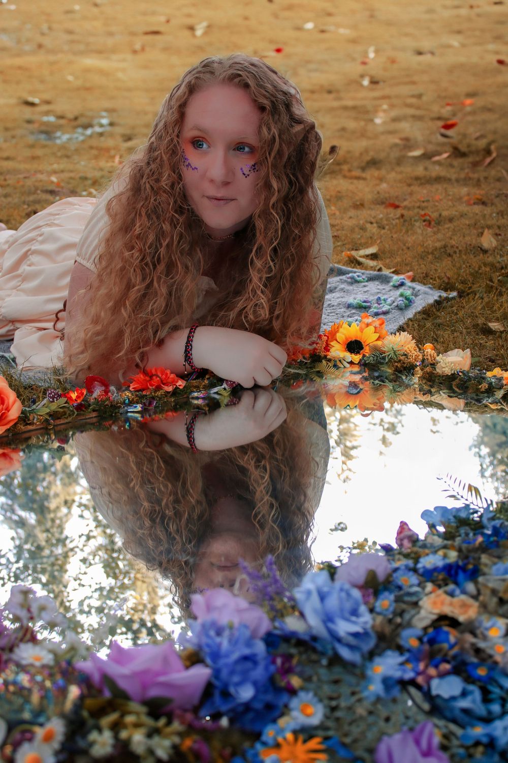 Artistic portrait captured with reflective surface surrounded by vibrant floral arrangements.