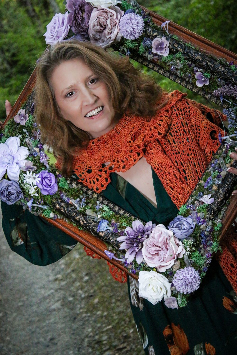 An ornate wooden frame decorated with purple and pink flowers showcases someone wearing an orange crochet shawl.