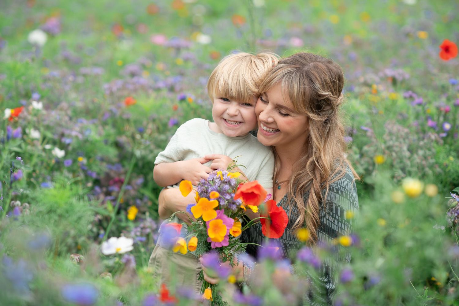 Mother and son laughing together in a beautiful wildflower meadow filled with colorful red and purple blooms.