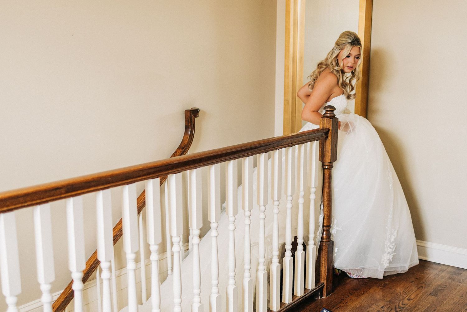 A white staircase baluster with decorative wooden railings and handrail curves around a corner in a neutral-colored interior.